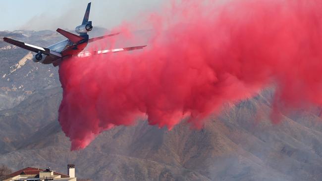 A person watches from a balcony as a firefighting aircraft drops the fire retardant Phos-Chek near homes during the Palisades Fire as wildfires cause damage and loss through Los Angeles County. Picture: Getty