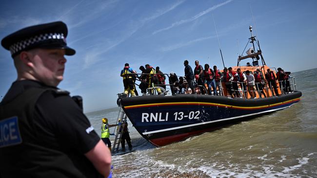 A British police officer stands guard as migrants disembark from a lifeboat after being picked up while trying to cross the Channel in 2022. Picture: Ben Stansall/AFP