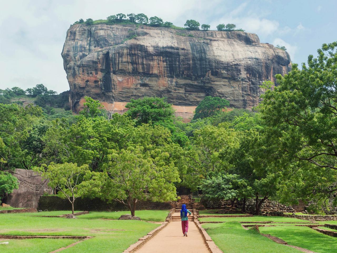 Lonely woman in headscarf walking to famous landmark Sigiriya rock with green trees forest around, Sri Lanka. UNESCO world heritage site