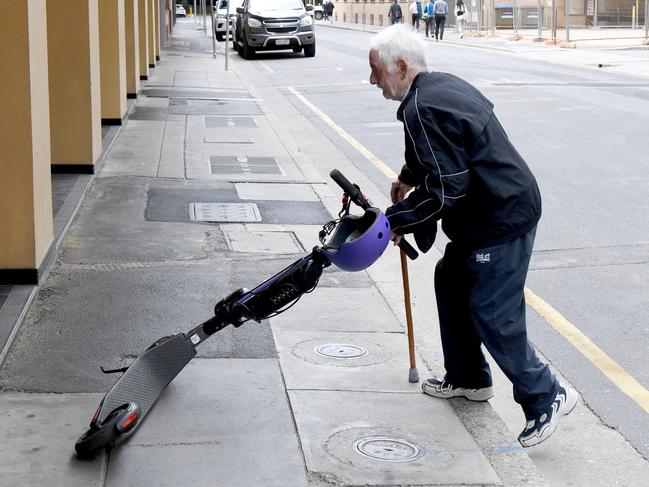 eScooters and eBikes city hazard. John Mete 80 from Victoria, tries to pick up an eScooter that was blocking the footpath pushing him on the road. The ebike was too heavy for him and when the eScooter alarm went off so he stopped moving it. Picture: Tricia Watkinson