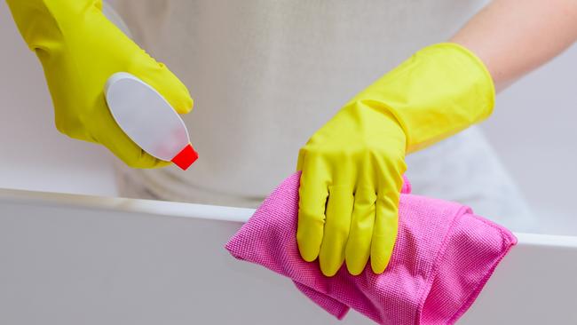 Female hands with yellow rubber protective gloves cleaning bath with pink cloth and spray detergent. Spring cleaning