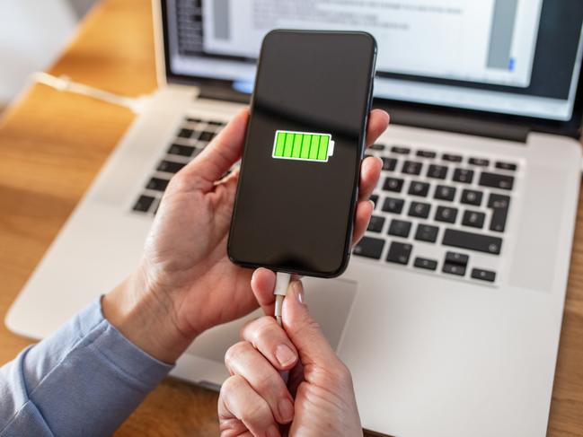 Woman removing charged smart phone with USB cable at laptop. work from home power