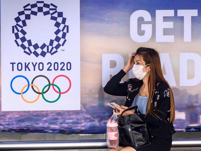 A woman wearing a facemask, amid concerns over the spread of the COVID-19 coronavirus, sits at a bus stop in front of a Tokyo 2020 Olympics advertisement in Bangkok on March 16, 2020. (Photo by Mladen ANTONOV / AFP)