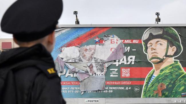 A military cadet stands in front of a billboard promoting contract army service in Saint Petersburg on October 5, 2022. - Russian President Vladimir Putin announced on September 21 a mobilisation of hundreds of thousands of Russian men to bolster Moscow's army in Ukraine, sparking demonstrations and an exodus of men abroad. (Photo by Olga MALTSEVA / AFP)