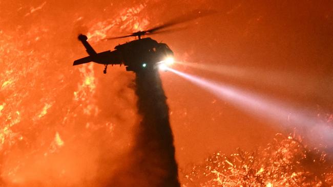 A fire fighting helicopter drops water as the Palisades fire grows near the Mandeville Canyon neighborhood and Encino, California, on January 11, 2025. The Palisades Fire, the largest of the Los Angeles fires, spread toward previously untouched neighborhoods January 11, forcing new evacuations and dimming hopes that the disaster was coming under control. Across the city, at least 16 people have died as multiple fires have ripped through residential areas since January 7, razing thousands of homes in destruction that US President Joe Biden likened to a "war scene." (Photo by Patrick T. Fallon / AFP)