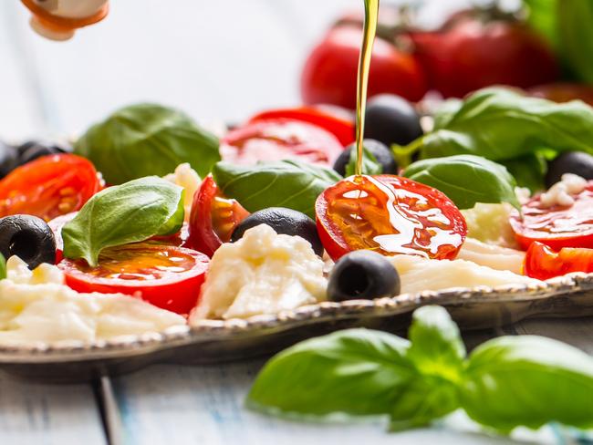 Pouring olive oil on caprese salad. Healthy italian or mediterranean meal.