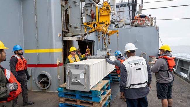 Civilian mariners aboard the USNS Washington Chambers attach a missile canister to a zip-line before it is transferred to the nearby USS Chosin. Picture: US Navy