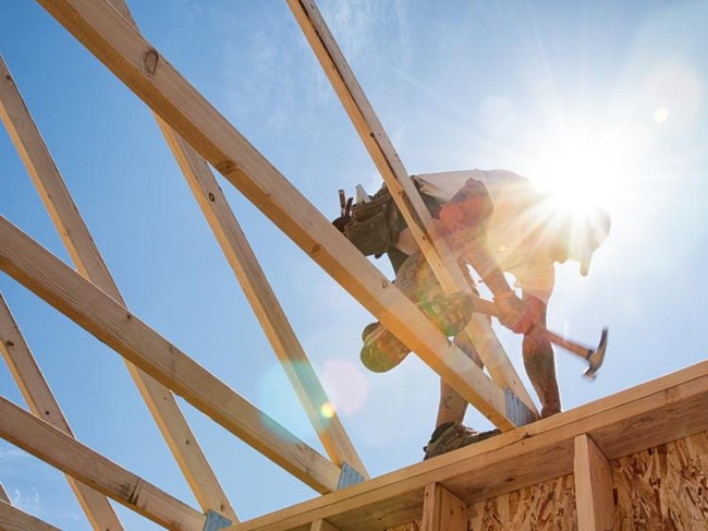 Construction worker framing a building against a sunny blue sky.