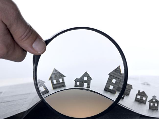 Hand holds the magnifying glass in front of an open newspaper with paper houses. That could mean rent, search, purchase real estate, property investment generic