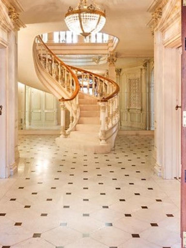 The sweeping spiral staircase was once the centrepiece of the home, rising from a grand entrance hallway beneath a detailed coffered ceiling.
