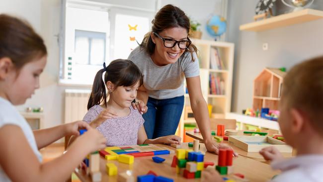 Preschool teacher with children playing with colorful wooden didactic toys at kindergarten