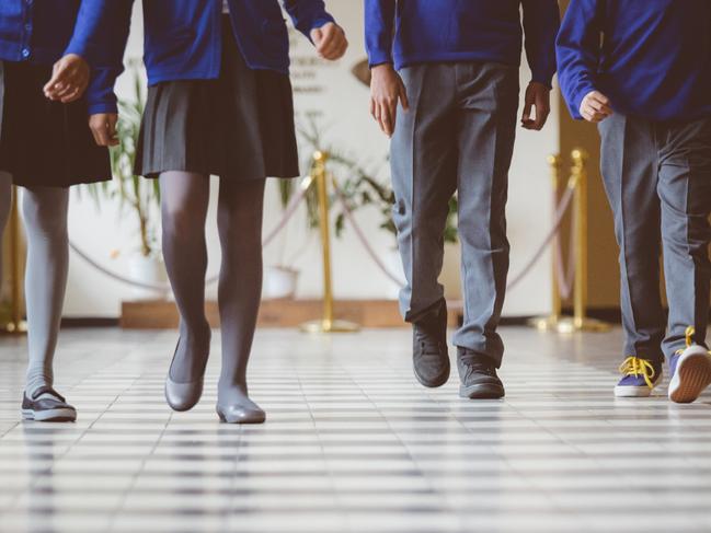 Cropped image of school kids in uniform walking together in a row through corridor. Focus on legs of students walking through school hallway.