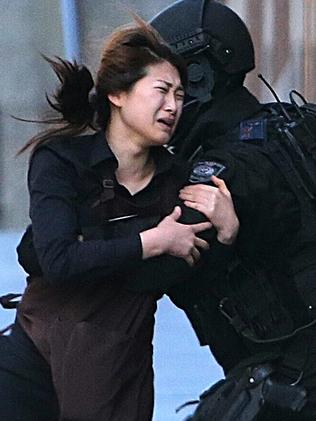 A hostage runs to armed tactical response police officers for safety after she escaped from a cafe under siege at Martin Place in the central business district of Sydney, Australia, Monday, Dec. 15, 2014. New South Wales state police would not say what was happening inside the cafe or whether hostages were being held. But television footage shot through the cafe's windows showed several people with their arms in the air. (AP Photo/Rob Griffith)