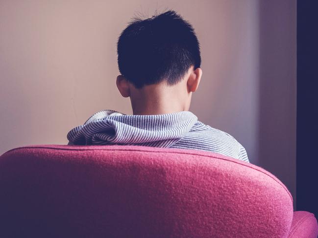 Sad preteen tween mixed Asian boy sitting alone in a big chair facing wall, depressed, autism awareness, children mental health concept