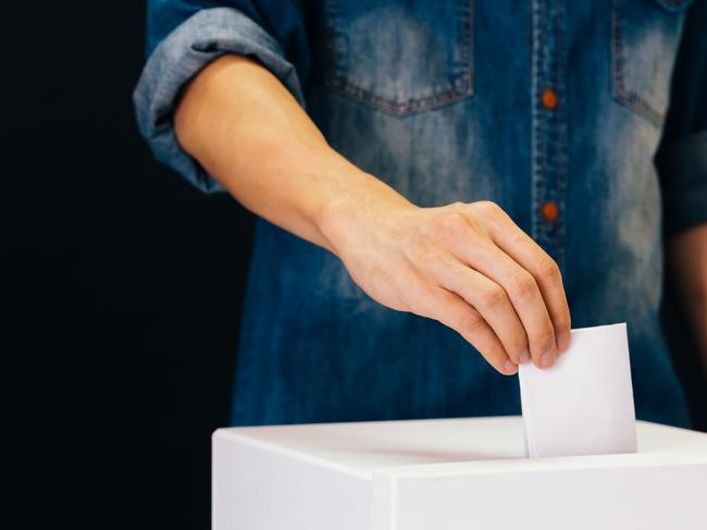 Front view of person holding ballot paper casting vote at a polling station for election vote in black background