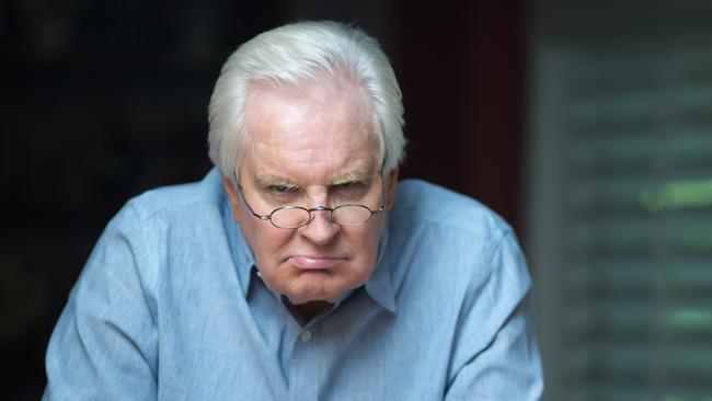 Grumpy old man staring at camera while sitting by the kitchen counter