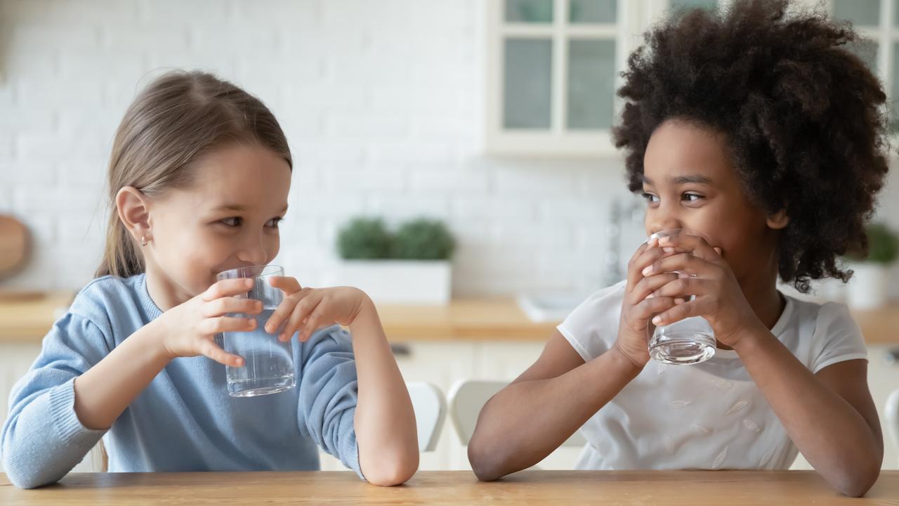 Little multiethnic girls drink mineral water at home