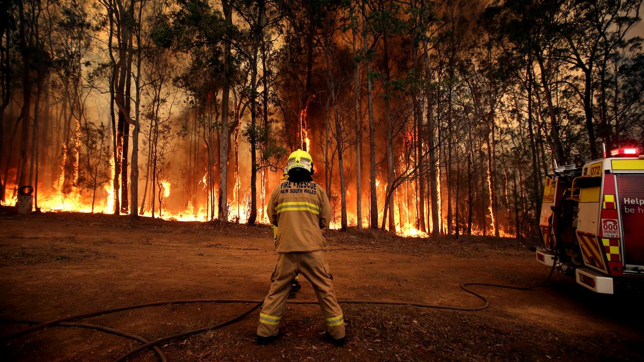 A firefighter holds back a blaze threatening a home at Tinonee near Taree on the NSW mid north coast. Picture: Nathan Edwards.