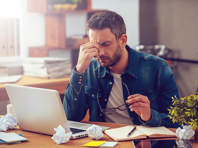 Frustrated young man massaging his nose and keeping eyes closed while sitting at his working place in office