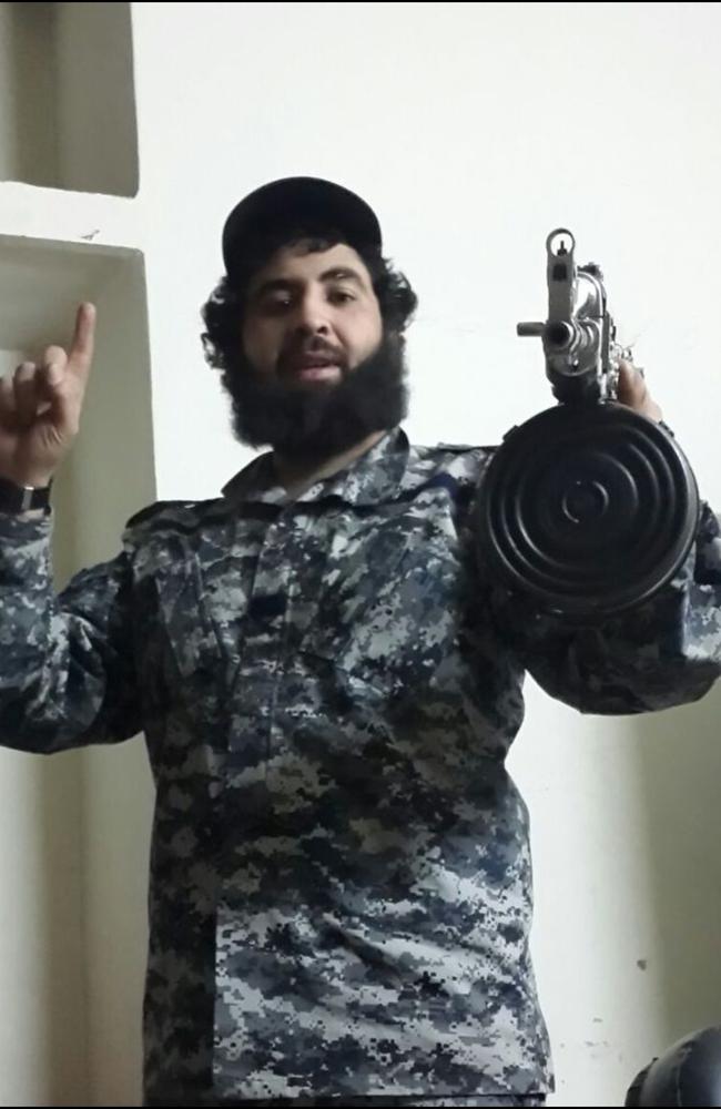 Clad in military fatigues, Sydney man Ahmed Merhi holds a large assault rifle while posing for a photo.