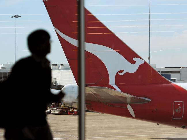 (FILES) This file picture taken on August 22, 2012 shows an airport passenger walking inside a terminal past the tail of a Qantas plane at the Sydney International Airport. - Australian flag carrier Qantas on August 20, 2020 posted an almost 2 billion USD annual loss after a "near-total collapse" in demand due to the COVID-19 coronavirus pandemic. (Photo by Greg WOOD / AFP)