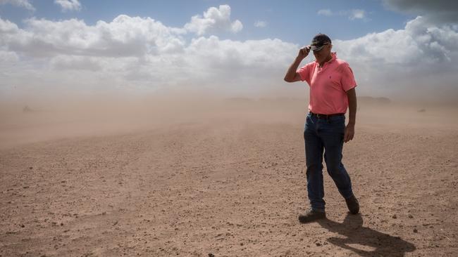 Dan Boland struggles to walk through a paddock as strong winds kick up a dust storm. Picture: Jake Nowakowski