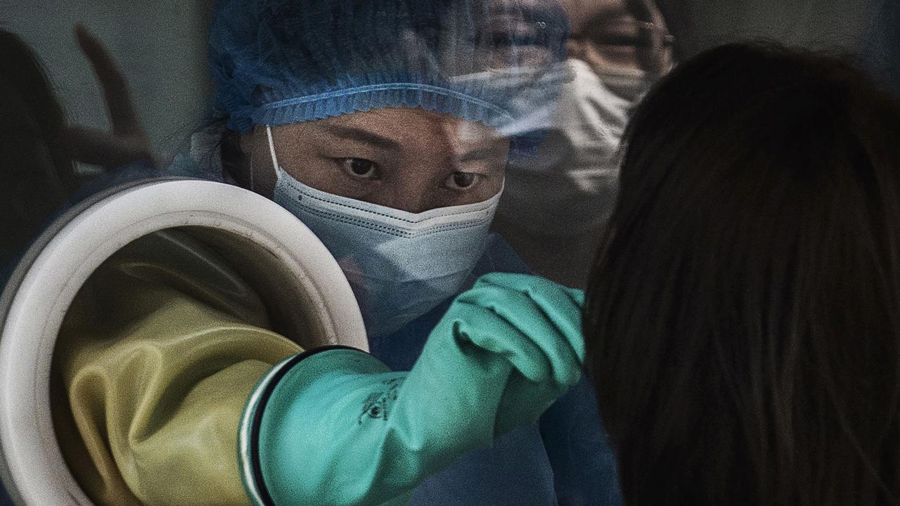 A medical worker wears protective clothing while performing a nucleic acid test on a client from behind glass at a testing site in Beijing, China. Picture: Kevin Frayer/Getty Images