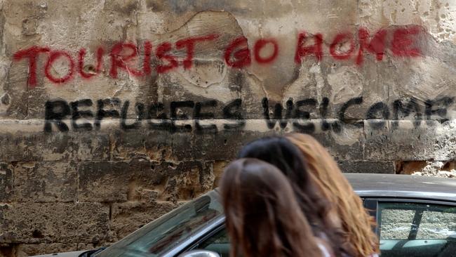 People walk past a graffiti in Palma de Mallorca, in the Spanish island of Mallorca, May 23, 2016. REUTERS/Enrique Calvo - RTX2ERQ3