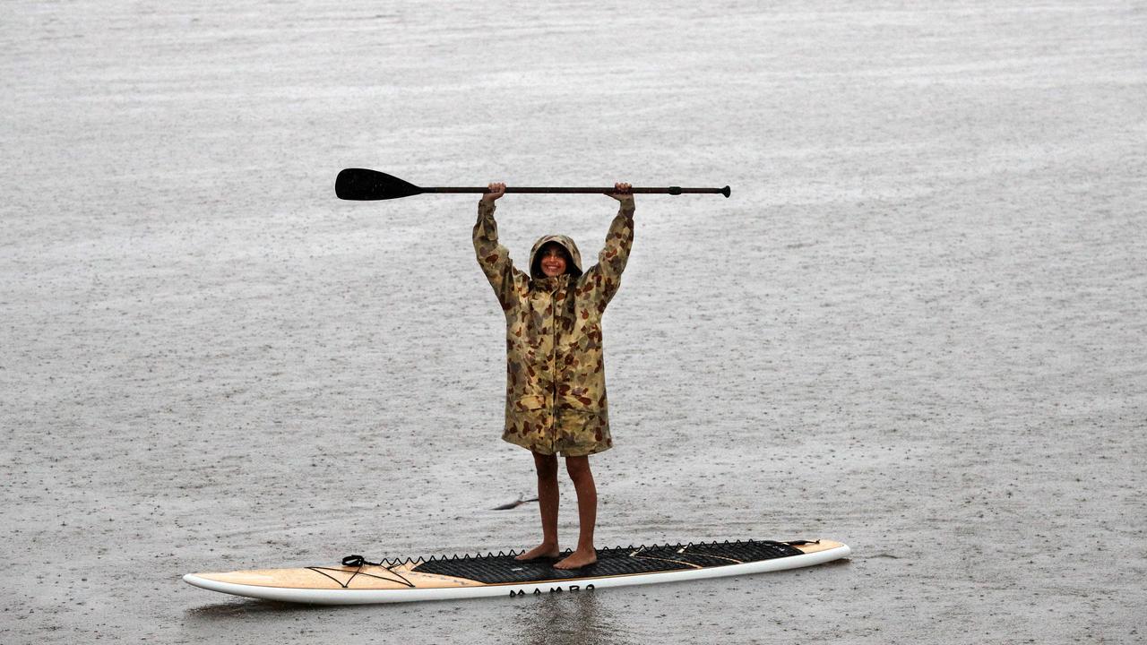 Amy Summer from Elanora takes a quick paddle to survey rising flood water on Nineteenth Ave lake as torrential rain falls over Queensland. Picture: NCA NewsWire / Scott Powick