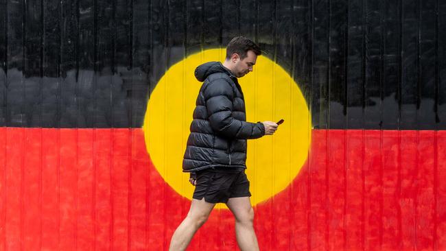 A pedestrian walks past a gate painted in the Aboriginal flag on the day of the referendum in South Yarra, Melbourne. Picture: Jake Nowakowski