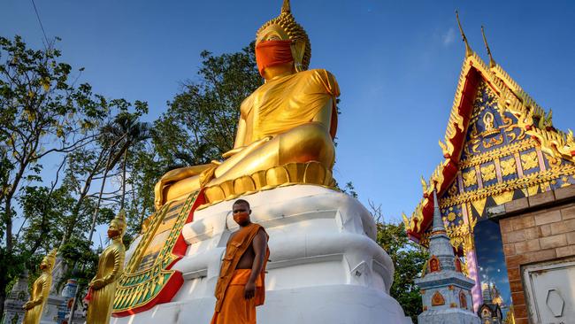 A monk walks in front of a giant Buddha statue wearing a face mask at Wat Nithet Rat Pradit temple in Pathum Thani outside Bangkok. Picture: AFP