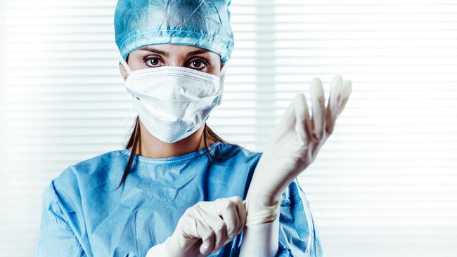 Portrait of Female doctor Surgeon in blue scrubs putting on surgical gloves and Looking at Camera