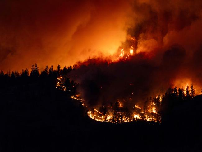 TOPSHOT - The McDougall Creek wildfire burns in the hills West Kelowna, British Columbia, Canada, on August 17, 2023, as seen from Kelowna. Evacuation orders were put in place for areas near Kelowna, as the fire threatened the city of around 150,000. Canada is experiencing a record-setting wildfire season, with official estimates of over 13.7 million hectares (33.9 million acres) already scorched. Four people have died so far. (Photo by Darren HULL / AFP)