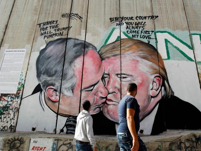 Palestinian locals walk past the mural depicting US President Donald Trump kissing Israeli Prime Minister Benjamin Netanyahu. Picture: AFP