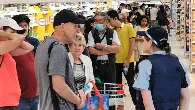 A police officer watches on as people queueing for a delivery of toilet paper, paper towel and pasta at a Coles supermarket in Sydney, Picture: James Gourley/AAP