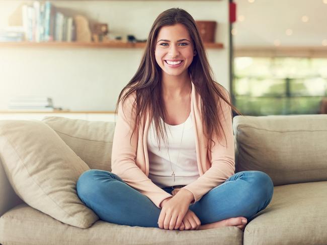 A cheerful young woman sitting at home on the couch. She has a mortgage on her first home. Picture: iStock.