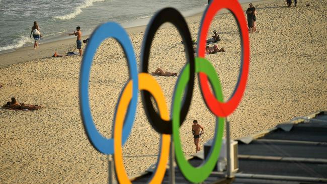 TOPSHOT — People are pictured walking along Copacaba beach through a set of Olympic rings, from during the men's beach volleyball qualifying match between Latvia and Cuba at the Beach Volley Arena in Rio de Janeiro on August 9, 2016, during the Rio 2016 Olympic Games. / AFP PHOTO / Leon NEAL