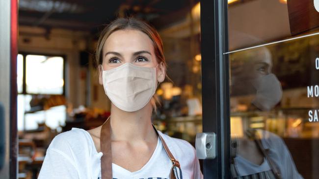 Happy business owner opening the door at a cafe wearing a facemask to avoid the spread of coronavirus ÃÂ¢Ãâ¬Ãâ reopening after COVID-19 concepts