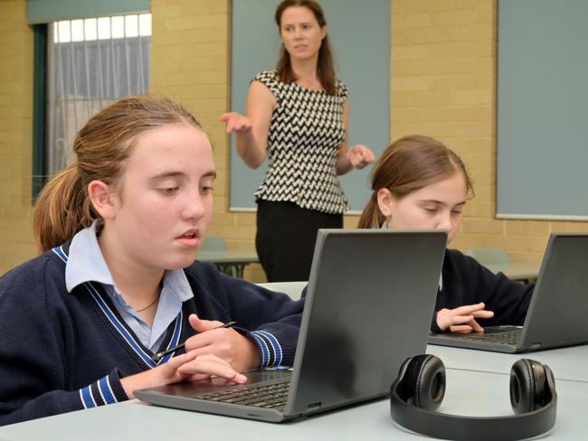 Technology teacher(Female  age 30-40) teaching schoolgirls how to use laptops in school classroom.