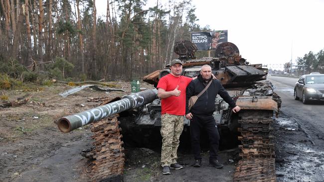 People stop on the road outside of Kyiv and take photographs beside a destroyed Russian tank.