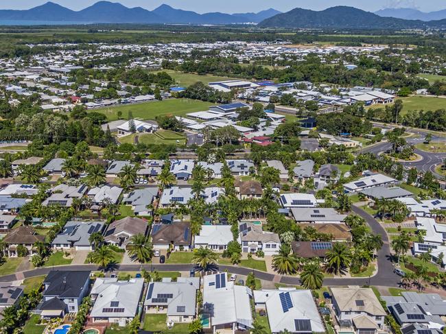 Developing Queensland - Aerial, wide angle view , looking down on established Cairns  suburb, reserve green space, Coral Sea & ranges in distance. Single level living with dwellings close together on housing blocks. Most houses with solar panels installed. Tropical climate, tropical trees, landscaped gardens.