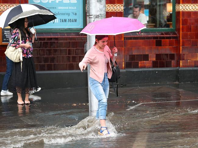 Pedestrians cross a flooded Flinders St. Picture: Ian Currie