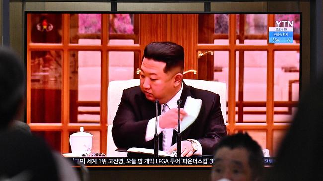 People sit near a screen showing a news broadcast of North Korea’s leader Kim Jong Un appearing in a face mask on television for the first time. Picture: AFP.