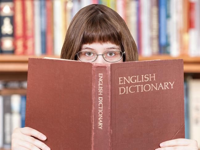 girl with spectacles looks over English Dictionary book and bookcase on background