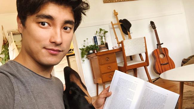 Remy Hii reading a book to his sister’s dog while he copes in isolation