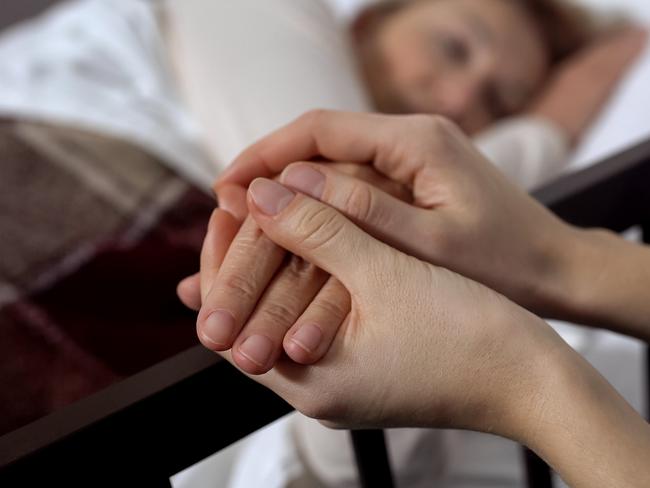 Daughter supporting her terminally ill mother lying on hospital bed, hospice istock image