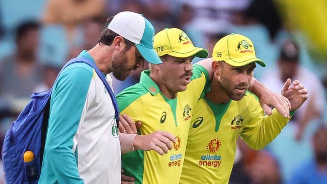 Australia's David Warner (C) is assisted by teammate Glenn Maxwell (R) and a trainer as he leaves the field after he suffered an injury during the one-day cricket match against India at the Sydney Cricket Ground (SCG) in Sydney on November 29, 2020. (Photo by DAVID GRAY / AFP) / -- IMAGE RESTRICTED TO EDITORIAL USE - STRICTLY NO COMMERCIAL USE --