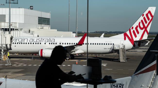 A man sits at a cafe in front of a Virgin Australia aircraft at Sydney Airport. Picture: AAP