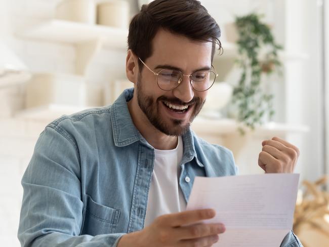 Head shot happy young man winner in eyeglasses reading paper letter with good news, making yes gesture. Joyful bearded guy celebrating personal achievement or banking loan approval, taxes refund.