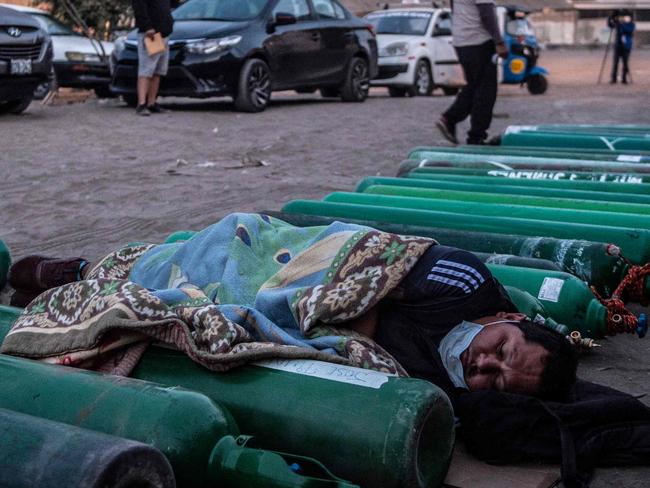 TOPSHOT - A person sleeps next to empty oxygen cylinders while waiting to refill it in Villa El Salvador, on the southern outskirts of Lima, on April 11, 2021, amid the COVID-19 coronavirus pandemic. - Relatives of COVID-19 patients are desperate for oxygen to keep their loved ones alive during a fierce second wave of the pandemic in Peru, on the day of the first round of presidential and parliamentary elections. (Photo by ERNESTO BENAVIDES / AFP)